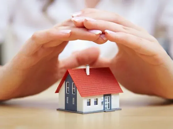 Mãos abrigando uma casa em miniatura sobre a mesa